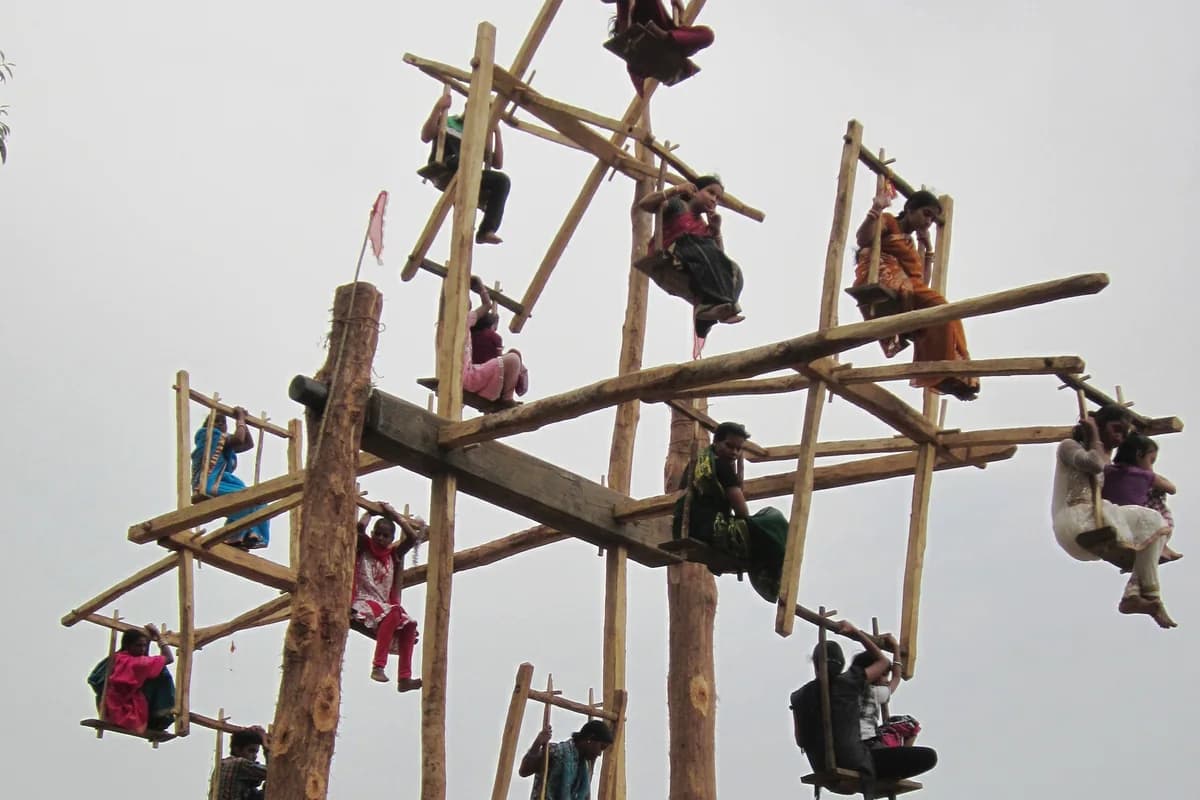 Decorated floral wooden rope swing suspended from tree branch for the 3-day Raja festival of Earth
